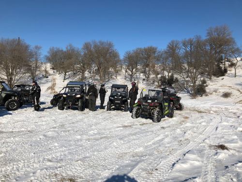 A group of people in winter gear stands beside several off-road vehicles on a snowy landscape.