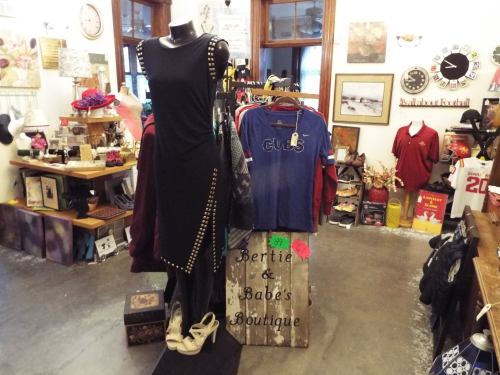 A boutique display featuring a black dress on a mannequin, clothing racks, and various accessories in a cozy shop.
