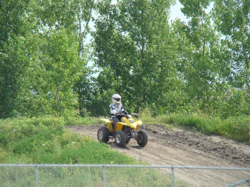 A person riding a yellow ATV on a dirt track surrounded by green trees and grass.