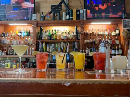 A bar counter displaying a variety of colorful cocktails and drinks, with shelves of liquor in the background.