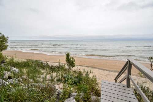 A serene beach scene with gentle waves, sandy shore, and a wooden walkway leading to the water under a cloudy sky.