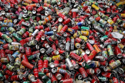 A chaotic pile of various empty soda cans in different colors and brands, including Coca-Cola and Fanta.