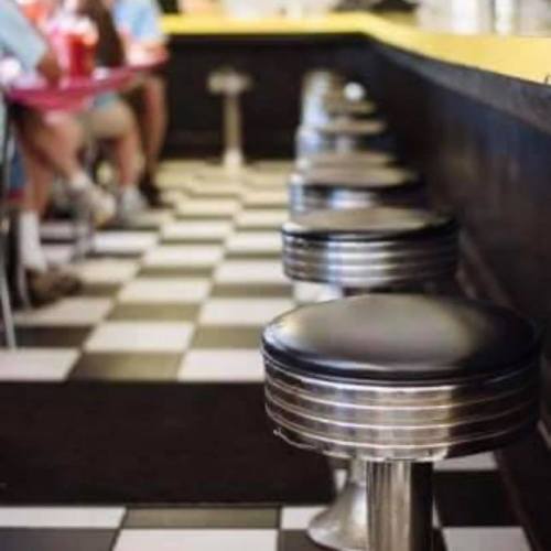 A retro diner interior featuring black and white checkered flooring and chrome bar stools along a counter.