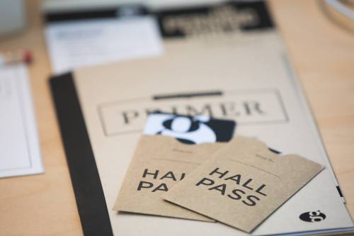 A close-up of a notebook with a "PRIMER" cover and two "HALL PASS" tickets on a wooden surface.