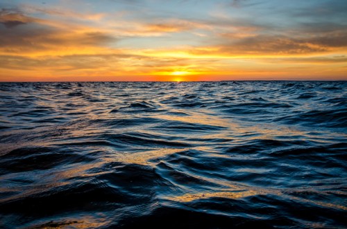A serene ocean at sunset, with gentle waves reflecting the warm colors of the sky.