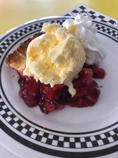 A slice of pie topped with vanilla ice cream and whipped cream, served on a checkered plate with berry filling.