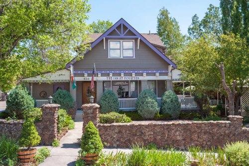 A charming gray house with purple accents, surrounded by greenery and a stone wall, featuring a welcoming porch.