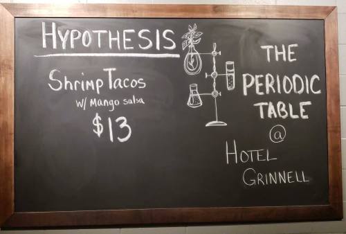 Chalkboard menu featuring shrimp tacos with mango salsa for $13 at Hotel Grinnell, titled "Hypothesis" and "The Periodic Table."