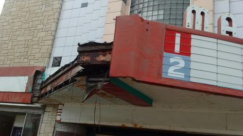 A weathered movie theater marquee with peeling paint and rust, displaying the numbers "1" and "2."