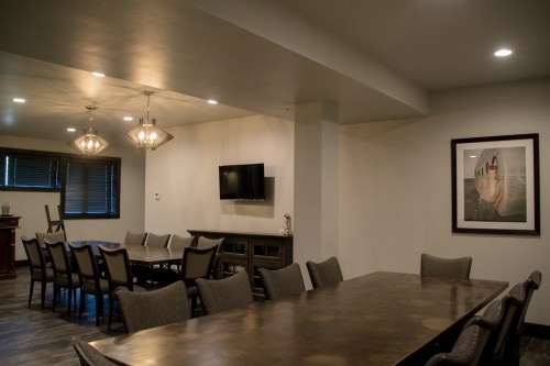 A modern meeting room with a long table, chairs, a TV, and a framed artwork on the wall. Soft lighting enhances the space.