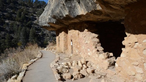 Ancient stone dwellings built into a cliffside, with a winding path leading through a natural landscape.