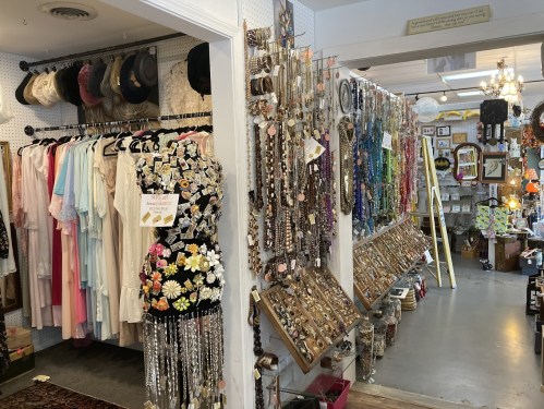 A colorful vintage shop interior featuring clothing racks and walls adorned with various jewelry and accessories.