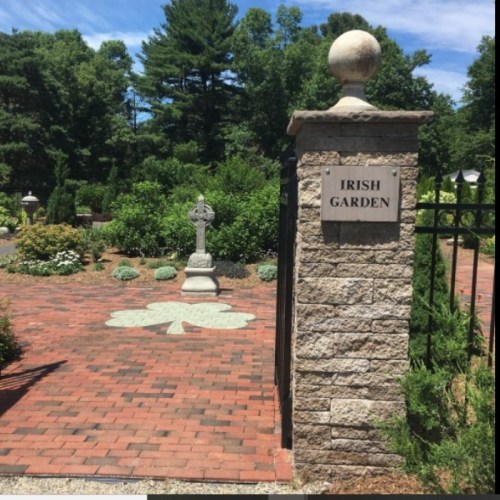 A stone entrance to the Irish Garden, featuring a Celtic cross and a clover design on the path, surrounded by greenery.