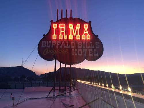 Neon sign for Irma Buffalo Bill's Original Hotel at sunset, with mountains in the background and a colorful sky.