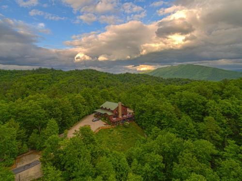 Aerial view of a rustic house surrounded by lush green trees and mountains under a cloudy sky.