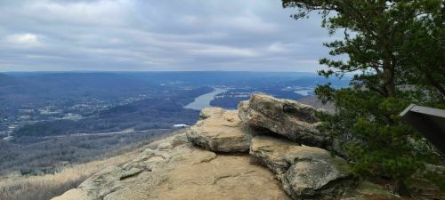 A rocky overlook with a view of a river winding through valleys and hills under a cloudy sky.