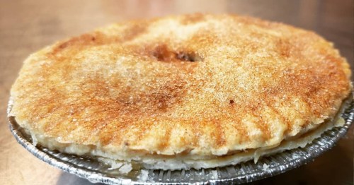 A golden-brown pie with a flaky crust, sitting in a silver pie tin, on a metallic surface.