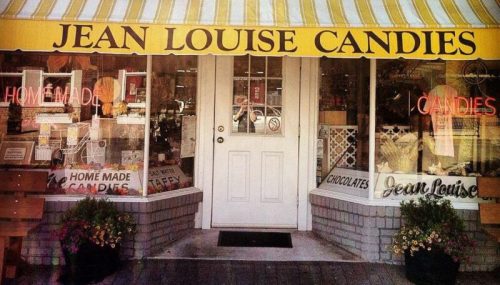 A storefront with a yellow awning, displaying "Jean Louise Candies" and signs for homemade chocolates and candies.