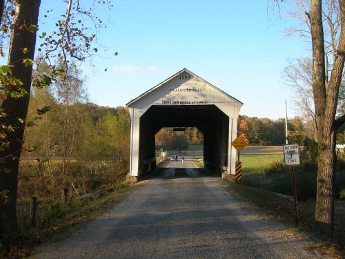 A covered bridge with a sign reading "1909" spans a rural road, surrounded by trees and fields.