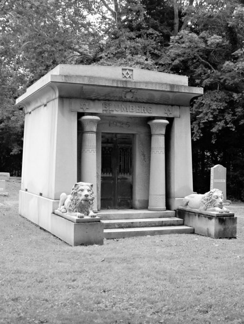 A stone mausoleum with lion statues at the entrance, surrounded by trees, in a cemetery. The year 1925 is inscribed.