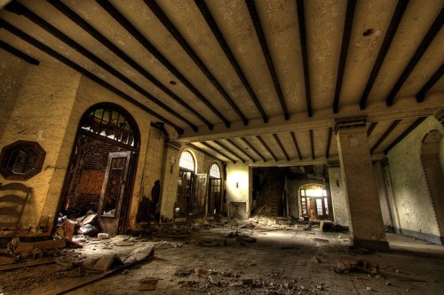 Abandoned interior of a building with dusty floors, exposed beams, and debris scattered throughout.