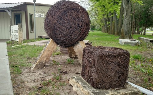 A large spherical sculpture and a smaller cube sculpture made of intertwined metal wire, set in a grassy area.