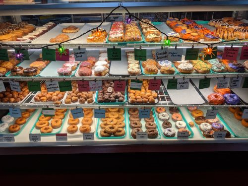 A display case filled with a variety of colorful donuts and pastries, labeled with names and prices.