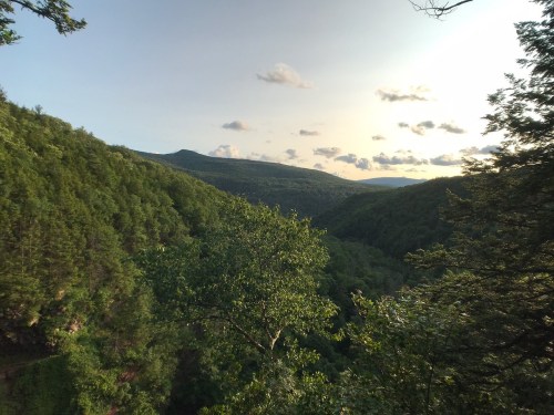 A scenic view of a lush green valley surrounded by mountains under a partly cloudy sky at sunset.
