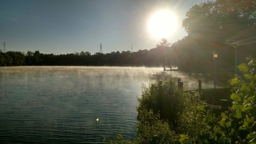 A serene lake at sunrise, with mist rising from the water and sunlight reflecting off the surface.