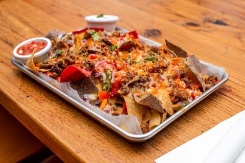 A tray of loaded nachos topped with cheese, meat, peppers, and onions, served with salsa and sour cream on the side.