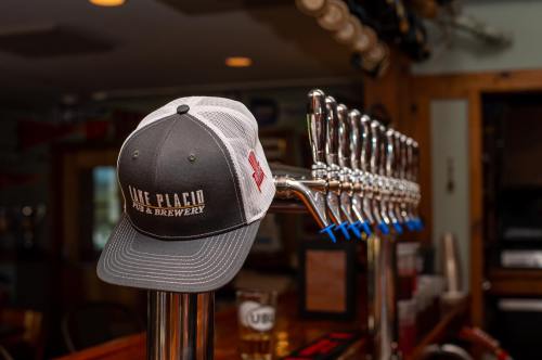 A gray and white cap with "Lake Placid Pub & Brewery" hangs on a beer tap in a cozy bar setting.