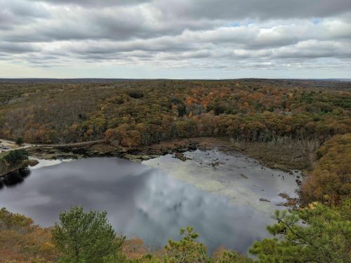 A scenic view of a lake surrounded by autumn-colored trees under a cloudy sky.