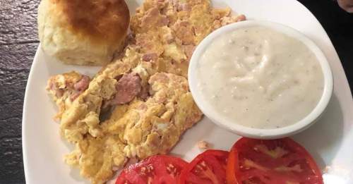 A plate with scrambled eggs, a biscuit, creamy gravy, and sliced tomatoes.