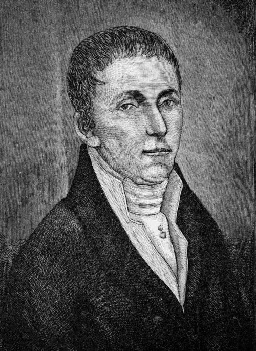 A black and white portrait of a young man in a formal coat and collar, looking directly at the viewer.