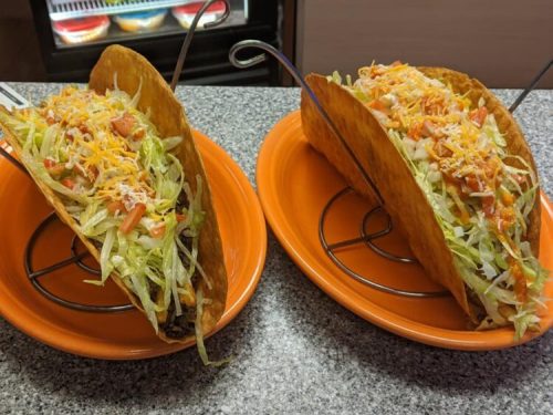 Two crispy taco shells filled with lettuce, tomatoes, and cheese, served on orange plates.