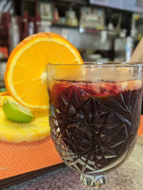 A close-up of a glass filled with a dark beverage, garnished with an orange slice and a lime wedge.