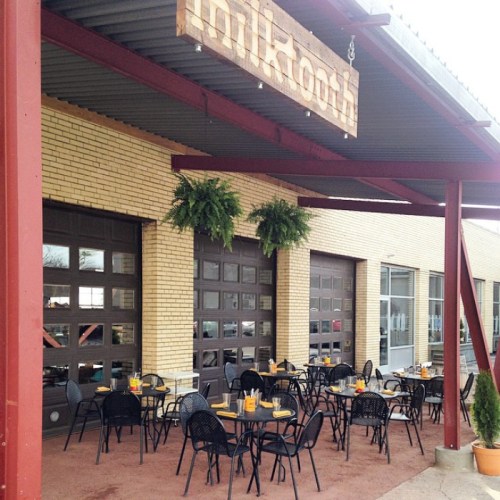 Outdoor seating area of a café with black tables and chairs, featuring a sign that reads "milktoth." Greenery hangs above.