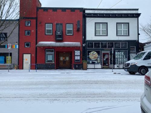 A snowy street scene featuring a red building and a white building with a cafe, both closed for the winter.
