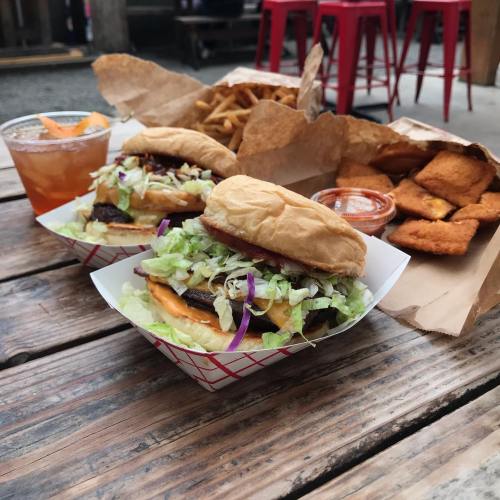 Two burgers with lettuce and toppings, a side of fries, chicken nuggets, and a drink on a wooden table.