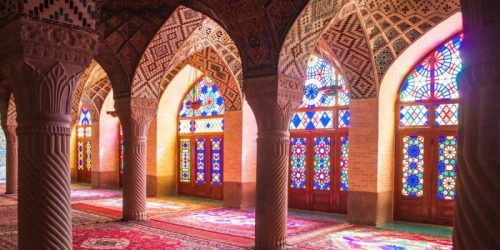 Colorful stained glass windows illuminate a beautifully patterned interior with arches and intricate designs.