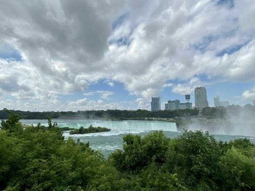 A scenic view of Niagara Falls with lush greenery and a cloudy sky in the background.