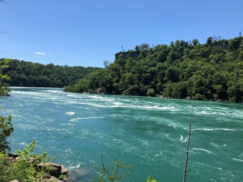 A vibrant turquoise river flows through a lush green landscape under a clear blue sky.