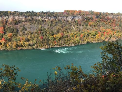 A scenic view of a river surrounded by colorful autumn foliage on the banks and cliffs above.