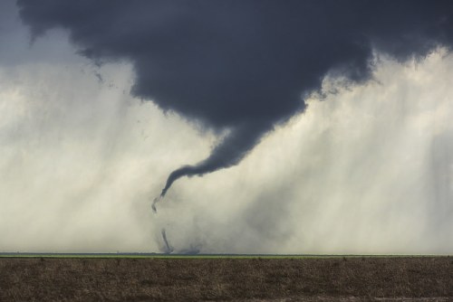 A dark tornado descends from stormy clouds over a flat, open landscape.