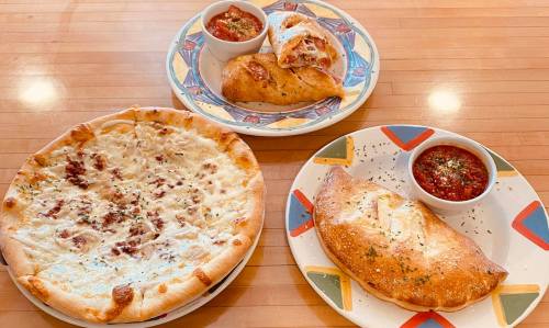 Two plates of Italian food featuring a cheese pizza, calzones, and marinara sauce for dipping.
