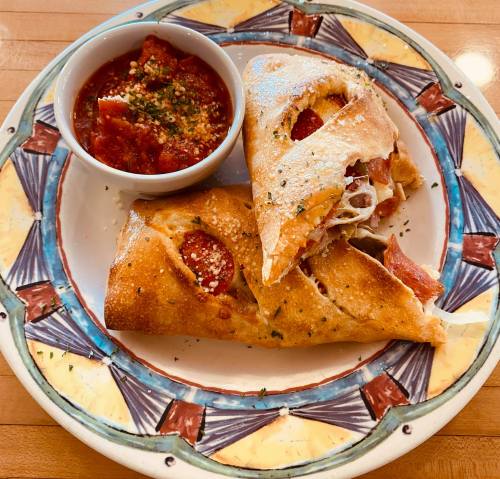 A plate with two folded calzones filled with pepperoni and cheese, served with a side of marinara sauce.
