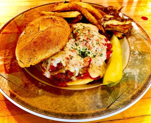 A plate featuring a cheesy meat sandwich, pickles, and crispy fries on a decorative dish.