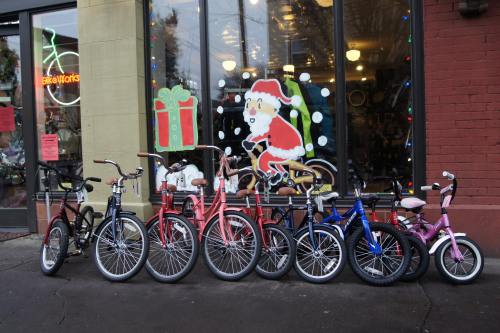 A row of colorful bicycles in front of a shop with festive holiday decorations and a Santa Claus window display.