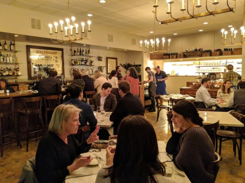 A bustling restaurant interior with diners at tables, a bar area, and staff serving food in a warm, inviting atmosphere.