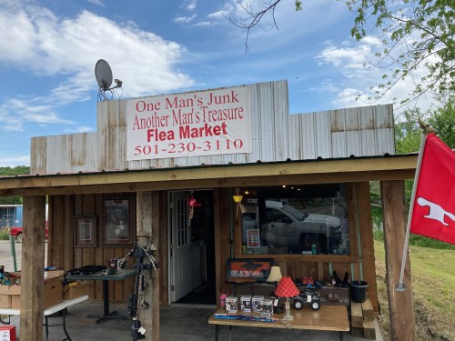 A rustic flea market with a sign reading "One Man's Junk, Another Man's Treasure" and various items displayed outside.
